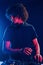 Man with curly hair using DJ equipment and standing in the dark neon lighted room