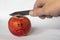 Man cuts a red apple with a knife. sad face image on an apple