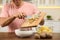 Man with cutting board and knife scraping vegetable peels into bowl on table in kitchen