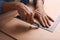 Man cutting chip board with utility knife and ruler at table, closeup