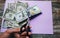 Man is cutting dollar banknotes with scissors on the purple pastel background. Money notes on the wooden  surface. Devaluation of