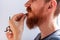 Man cutting his own beard and mustache with scissors and comb. Caucasian red bearded male trimming hair on face at home