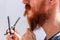 Man cutting his own beard and mustache with scissors and comb. Caucasian red bearded male trimming hair on face at home