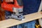 Man cutting a plank with a jigsaw machine sawing wood board