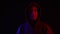 Man in dark hoodie looking up to camera on black background in blue and red lighting. Portrait mysterious man in hood in