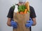 A man from a delivery service holds a package with groceries close-up on a white background. Courier wearing blue gloves