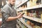 Man is in the department of canned vegetable supermarket and uses a smartphone. Buyer looks at the shopping list on the smartphone