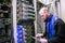 A man with a digital tablet working in a server room. The engineer stands next to a multitude of internet wires. The technician