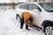 A man digs out a stalled car in the snow with a car shovel. Transport in winter got stuck in a snowdrift after a snowfall, sat on