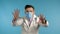 Man in doctor medical coat and protective mask showing frightening gesture, trying to scare. Blue studio background