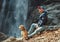 Man with dog sitting near waterfall