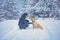 The man with the dog sitting in a snowy pine forest