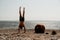 Man doing yoga exercise outdoors standing on old rusty floating marine mine on the beach with rocky shore and sea