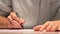 Man is drawing or writing on white sheet of paper. Macro shot of business wearing a shirt and writing on paper behind the desk