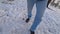 Man dressed in blue jeans walks in the snow on a winter day, legs close up, a wide angle,