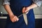 A man dressed in a blue kitchen apron sharpens the blade of a knife with a whetstone before starting to cook. Kitchen utensils