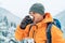 Man drinking a hot drink from thermos flask dressed bright orange softshell jacket while he trekking winter mountains route.