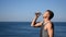 A man drinking and pours water on his face from a plastic bottle on the ocean, refreshing after a workout