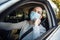 A man drives a car and adjusts medical mask during coronavirus outbreak. Taxi driver delivers his passanger to the destination.