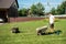 Man is driving a wheelbarrow into which he will collect mowed grass from a lawn mower.