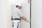 Man drywall worker installing plasterboard sheet to wall. Wearing hardhat, work gloves, safety glasses and tool belt. Isolated on