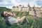Man with earphone lies on the ground and looking at old castle and eating an apple
