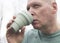 Man with eco reusable coffee cup or silicon tea mug and drinking, close up