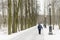 The man is an elderly pensioner standing in the park in the winter. High trees, bench, lantern.