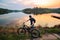 Man with an electric fatbike on the background of a lake and sunset. Picturesque place in the village. Concept of a healthy