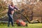 Man with electric lawnmower, lawn mowing. Gardener trimming a garden. Sunny day, suburb, village.