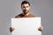 Man with empty blank banner ad on studio background. Portrait of attractive man holding empty blank poster. Man showing