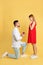 Man with engagement ring making marriage proposal to girlfriend on yellow background