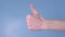 Man enters his hand into the frame showing the thumb raised up. A man`s hand shows a like sign on blue background