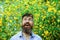 Man with excited expression in blooming garden with tall yellow flowers, happiness concept. Male florist having fun in