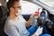 Man with face mask and rubber gloves using spray bottle sanitizer to protect car steering wheel from bacteria. Antiseptic, hygiene