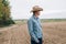 Man farmer agronomist in jeans and shirt stands back in field after haymaking  with tablet looking into the distance. Rural