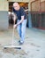 Man farmer cleaning floor with mop at horse stabling