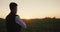 A man farmer looks into the distance at his field, stands alone at sunset.