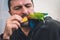 Man feeds green parrot with mouth, parrot agapornis roseicollis