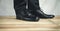 Man feet in black leather shoes stands on wooden floor.