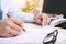 Man is filling paperwork with pen. Picture of computer, keyboard, glasses and notepad