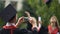 Man filming best friends throwing graduation caps into air and posing for camera