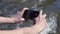 Man filming river on phone. Clip. Close-up of hands with phone on background of swirling muddy river. Person in nature