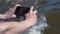Man filming river on phone. Clip. Close-up of hands with phone on background of swirling muddy river. Person in nature