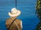 Man fishing with a cane, sitting on rocks with a straw hat on his back.