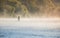 Man fishing in river with fly rod during summer morning.