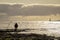 Man fishing silhouetted against a bright golden sea with roker pier and lighthouse blurred in the background.