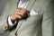 Man fixing handkerchief in breast pocket of his suit on grey background, closeup
