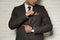 Man fixing handkerchief in breast pocket of his suit near white brick wall