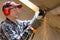 Man fixing metal frame using angle grinder on attic ceiling covered with rock wool